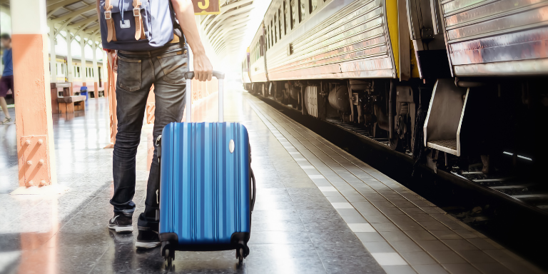 Ein Mann steht mit einem Rollkoffer am Bahnhof