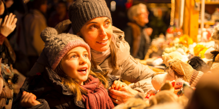 Une mère et son enfant sur un marché de Noël, tous deux souriants.