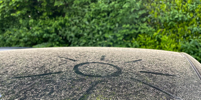 Soleil dessiné dans la poussière de pollen sur une voiture